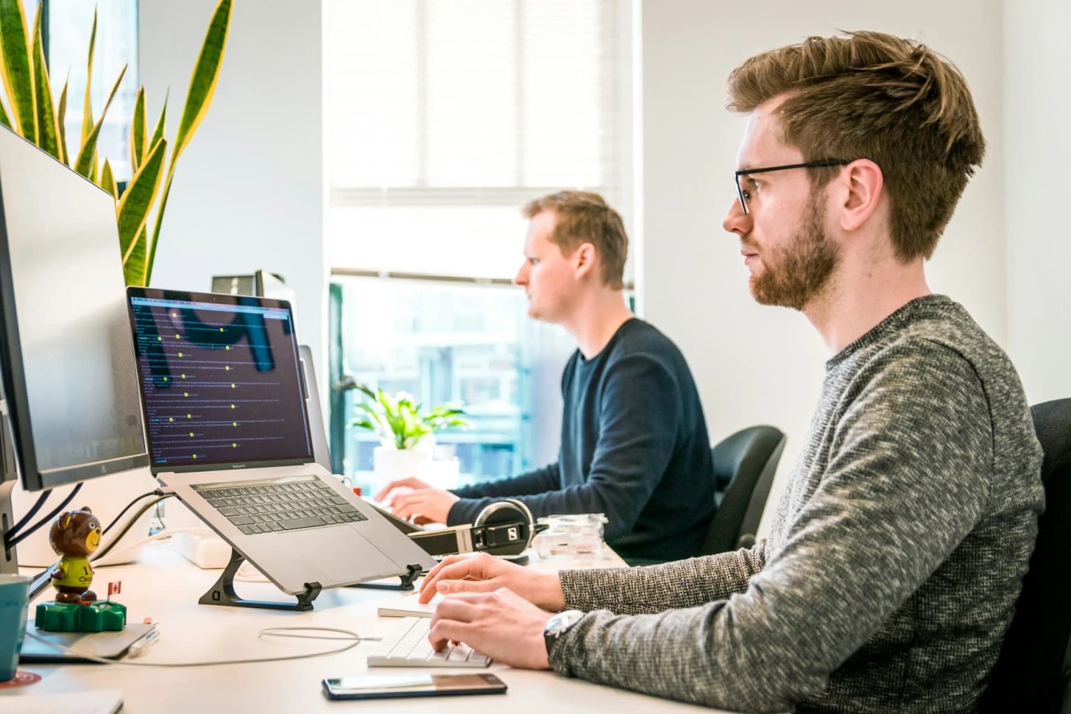 Managed IT Service, Mann mit Laptop vor Bildschirm am Arbeitsplatz